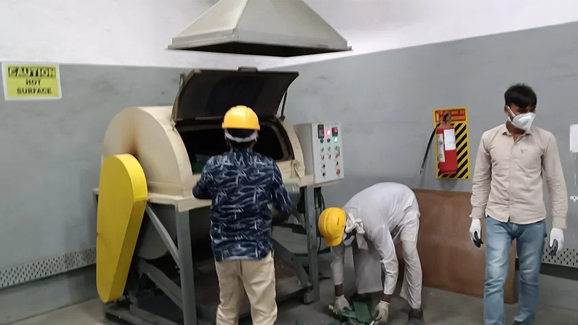 Workers in safety helmets operating a processing machine under an extraction hood